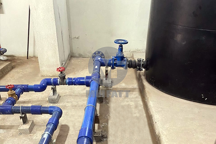 A network of blue pipes connected to a black PE tank supported by a concrete slab base, ensuring secure water distribution indoors.