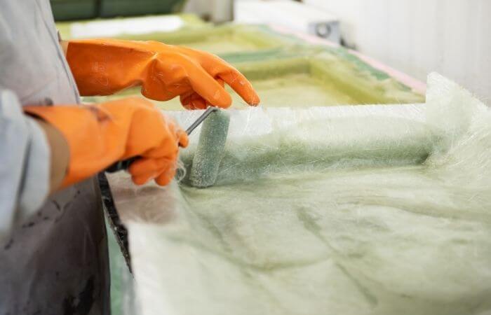 Hand of a Factory Worker in a glove rolling chemical solution with a tool on a fiberglass mold.