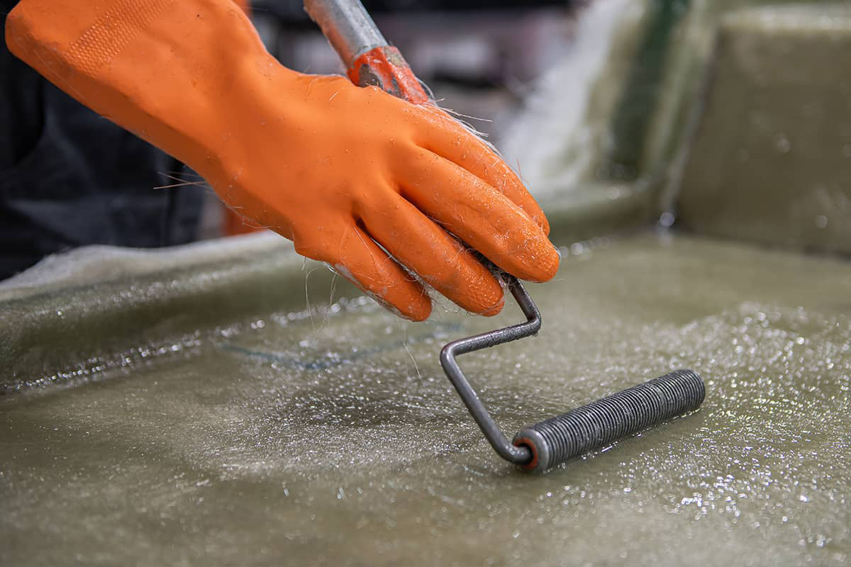 Hand of a Factory Worker in a glove rolling chemical solution with a tool on a fiberglass mold.