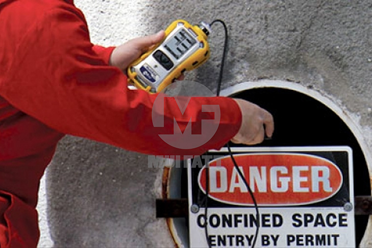 Authorized gas tester using digital meter at tank entry point with confined space warning sign