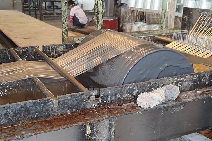 Fiberglass rovings passing through resin bath as part of filament winding preparation process for FRP tanks.